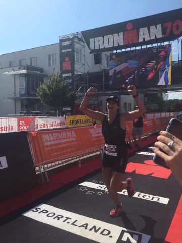 Woman crossing a finish line at an ironman event, celebrating with her hands above her head