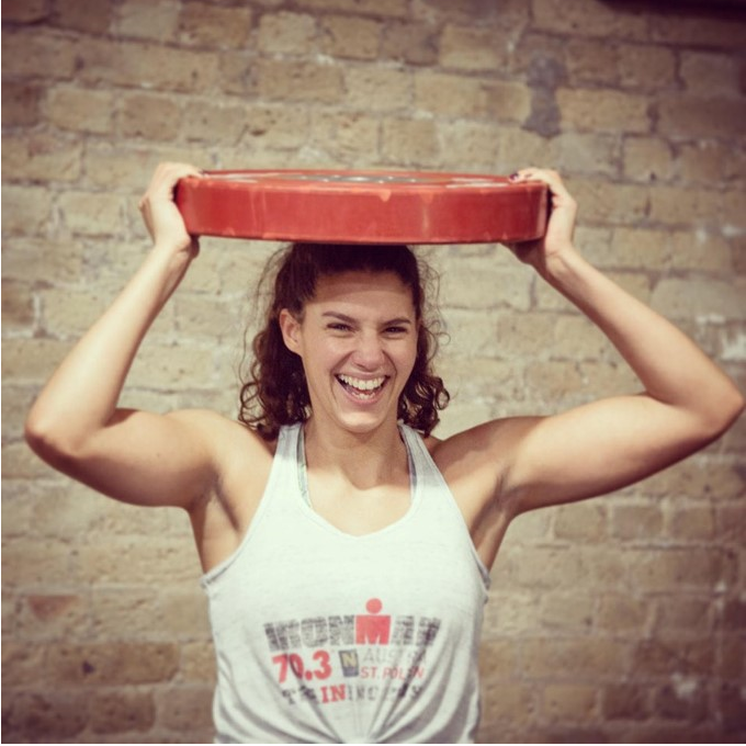 Girl in personal training session laughing while holding a red weight plate on her head